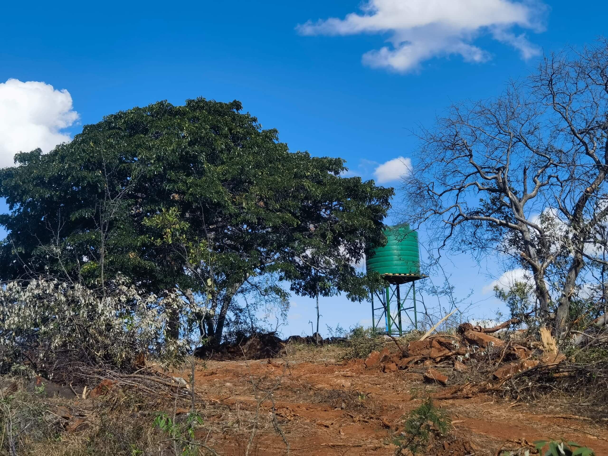 Elevated green water tank on steel stand, rural landscape, Batanai Community